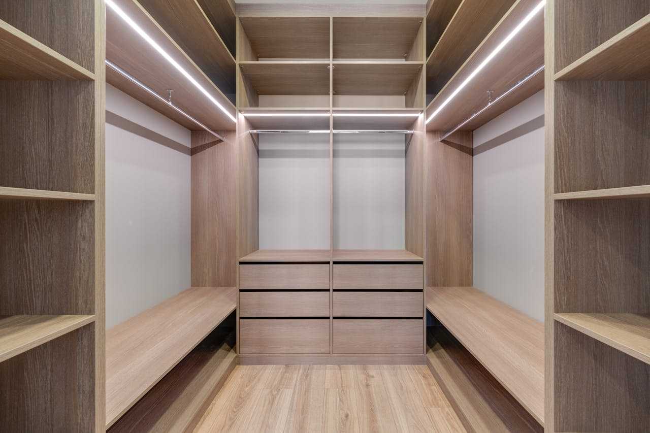 hero-img-02 Spacious walk-in closet with wooden shelves and LED lighting creates a minimalist and modern design.