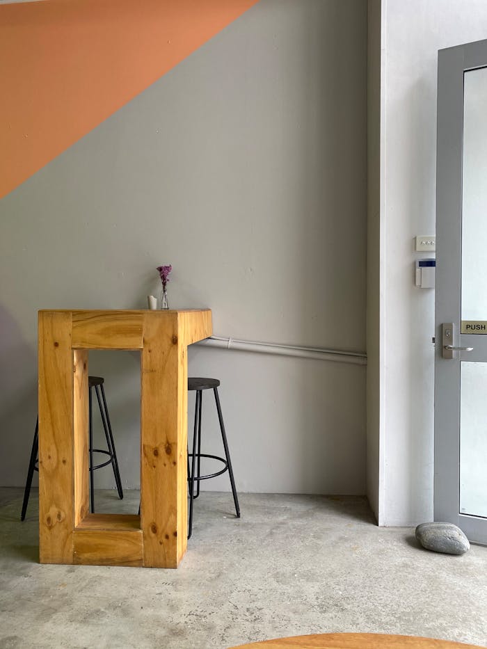our-services-3 A minimalist apartment corner with a wooden table, stools, and a vase on concrete floor.
